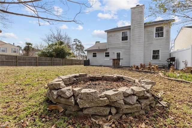 rear view of property featuring a fenced backyard, a yard, and a chimney