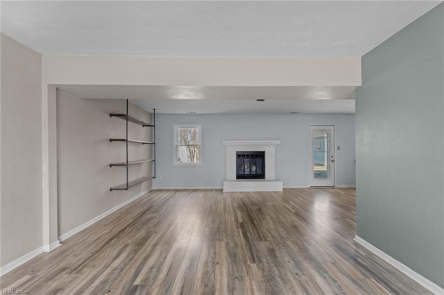 unfurnished living room featuring a glass covered fireplace, baseboards, and wood finished floors