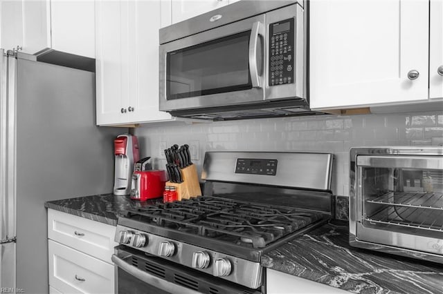 kitchen with a toaster, white cabinetry, appliances with stainless steel finishes, backsplash, and dark stone counters