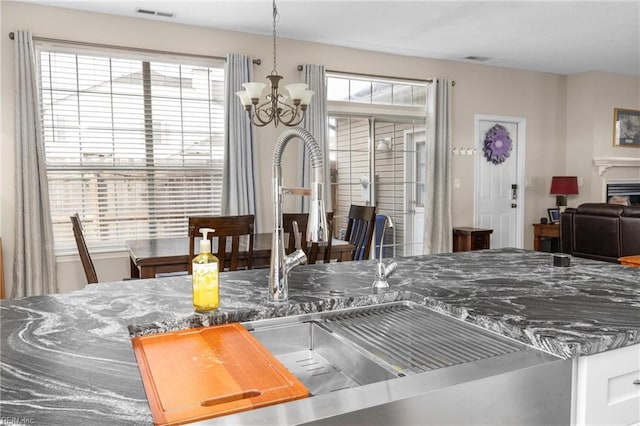 kitchen with visible vents, a sink, dark stone countertops, and an inviting chandelier