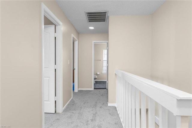 hallway featuring baseboards, visible vents, a textured ceiling, and carpet flooring