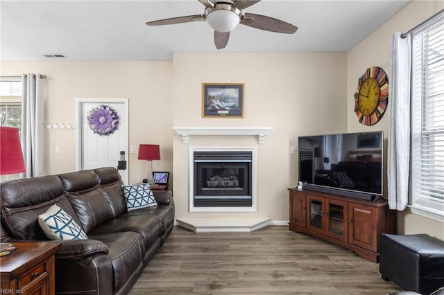 living area with visible vents, a fireplace with raised hearth, ceiling fan, wood finished floors, and a textured ceiling