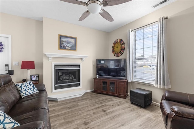 living room with light wood-type flooring, visible vents, a fireplace with raised hearth, and baseboards