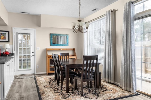 dining area featuring an inviting chandelier, light wood-style flooring, visible vents, and a textured ceiling