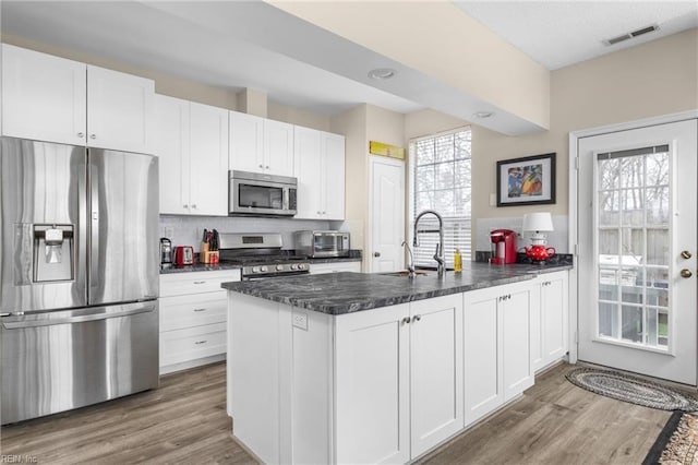 kitchen featuring visible vents, white cabinets, appliances with stainless steel finishes, a peninsula, and a sink