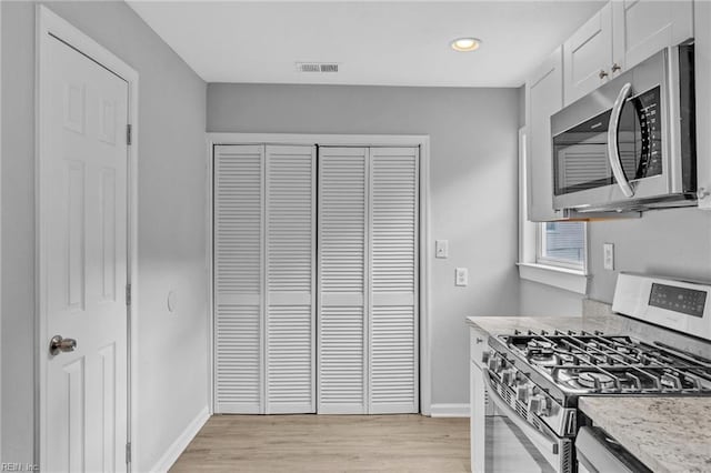 kitchen with stainless steel appliances, visible vents, baseboards, white cabinets, and light wood-style floors