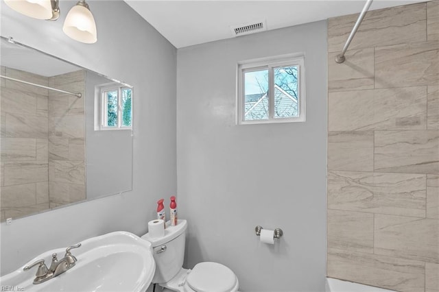 bathroom featuring toilet, visible vents, a sink, and tiled shower