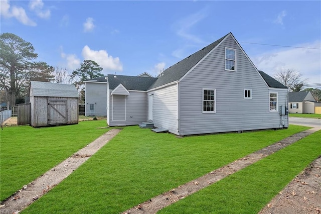 rear view of house featuring a storage shed, a shingled roof, a yard, and an outdoor structure