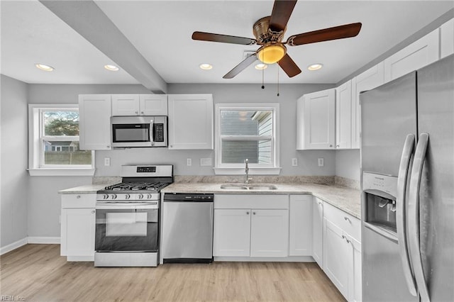 kitchen with appliances with stainless steel finishes, light wood-type flooring, a sink, and white cabinets