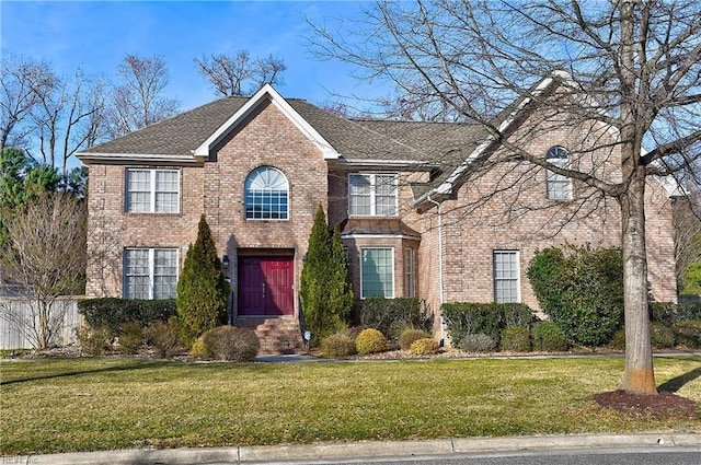 view of front of house featuring a front yard, brick siding, and roof with shingles