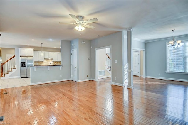 unfurnished living room with decorative columns, light wood finished floors, visible vents, stairway, and a ceiling fan