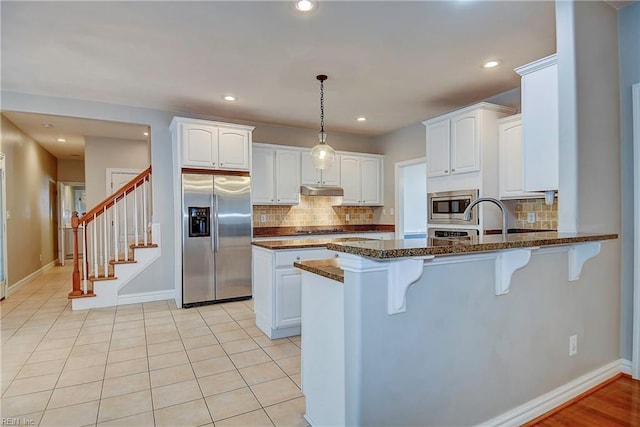 kitchen with appliances with stainless steel finishes, white cabinets, dark stone counters, a peninsula, and a kitchen breakfast bar