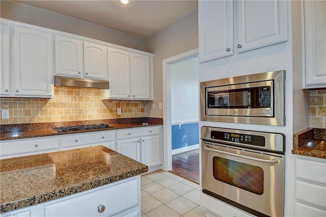 kitchen with stainless steel appliances, dark stone countertops, white cabinets, and under cabinet range hood