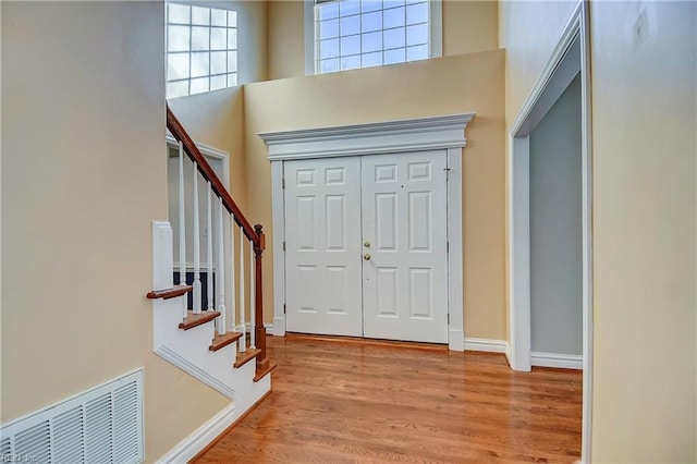 entrance foyer with a high ceiling, wood finished floors, visible vents, baseboards, and stairway