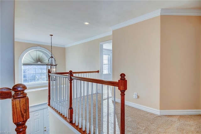 hallway with carpet floors, an upstairs landing, baseboards, ornamental molding, and an inviting chandelier