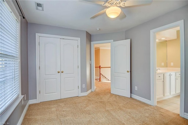 unfurnished bedroom with a closet, light carpet, baseboards, and ensuite bath