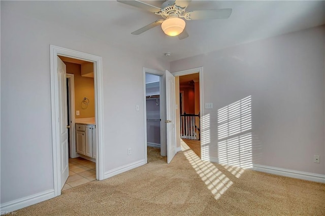 unfurnished bedroom with light colored carpet, baseboards, a closet, a walk in closet, and ensuite bath