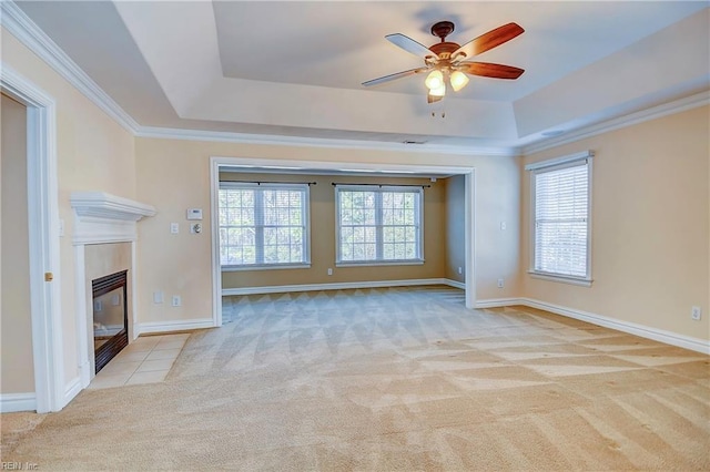 unfurnished living room featuring a tile fireplace, carpet floors, baseboards, ornamental molding, and a tray ceiling