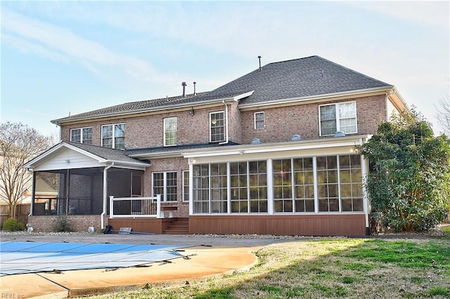 back of house with brick siding, a shingled roof, a sunroom, a lawn, and a covered pool