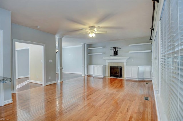 unfurnished living room with light wood finished floors, visible vents, a ceiling fan, a tile fireplace, and ornate columns