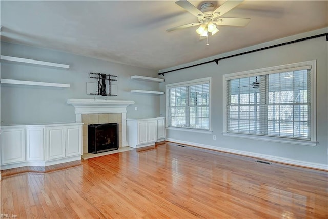 unfurnished living room featuring light wood-style floors, visible vents, a ceiling fan, and a tiled fireplace