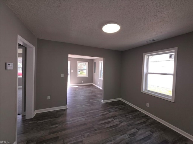 unfurnished room featuring a textured ceiling, dark wood-style flooring, visible vents, and baseboards