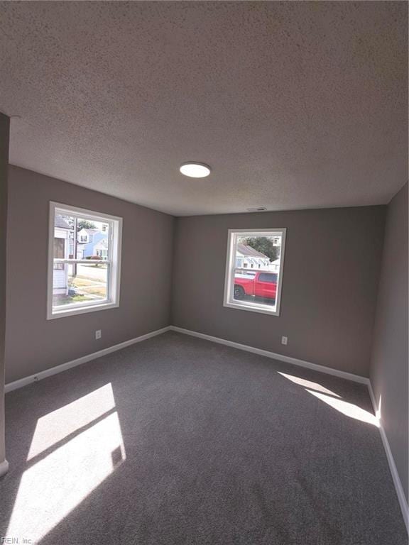 unfurnished room with dark carpet, a textured ceiling, and baseboards