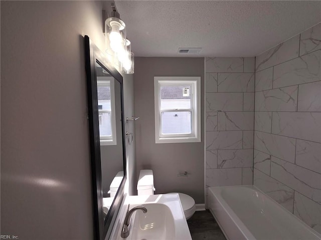 full bathroom featuring baseboards, visible vents, toilet, a textured ceiling, and a sink