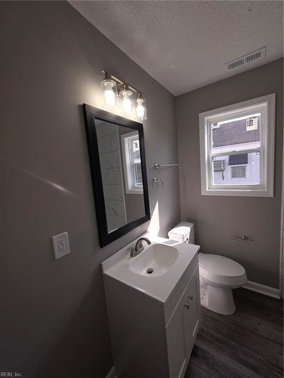 half bathroom with a textured ceiling, toilet, wood finished floors, vanity, and visible vents