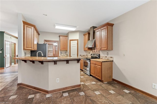 kitchen featuring wall chimney exhaust hood, stone finish floor, appliances with stainless steel finishes, a breakfast bar, and a peninsula