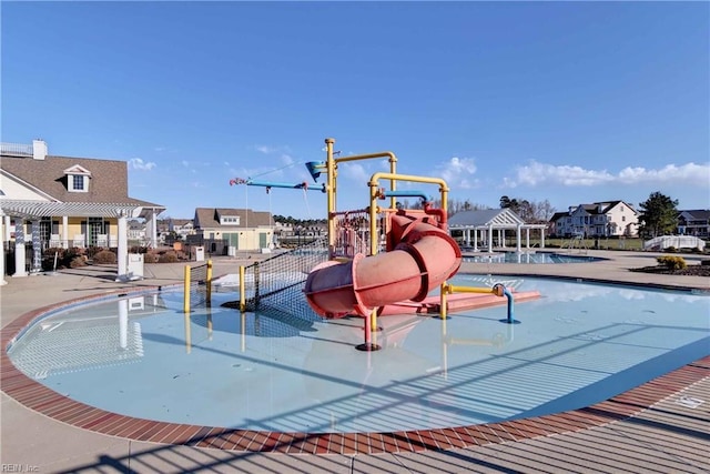 community pool with a water slide, a patio area, a water play area, and a residential view