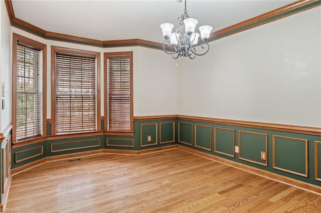 unfurnished room with visible vents, a wainscoted wall, light wood-style flooring, an inviting chandelier, and crown molding