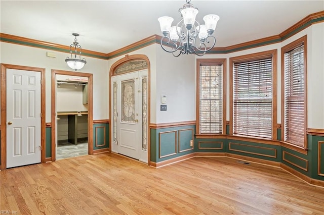 unfurnished dining area featuring visible vents, a wainscoted wall, wood finished floors, crown molding, and a decorative wall