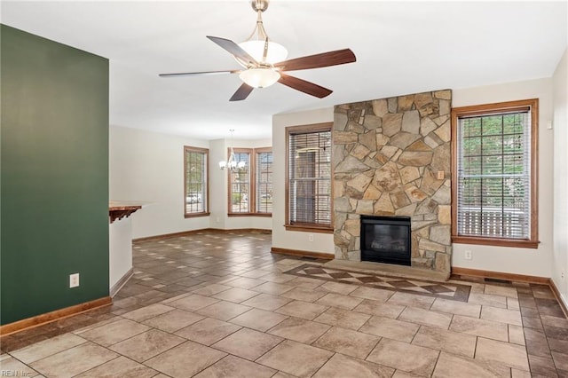 unfurnished living room with ceiling fan with notable chandelier, a stone fireplace, baseboards, and tile patterned floors