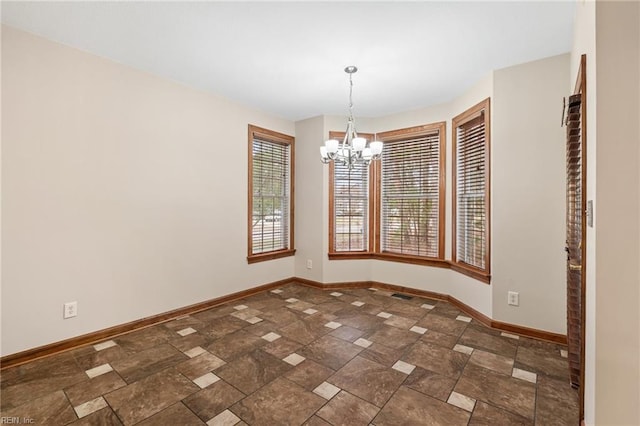 unfurnished room featuring stone finish floor, baseboards, and an inviting chandelier