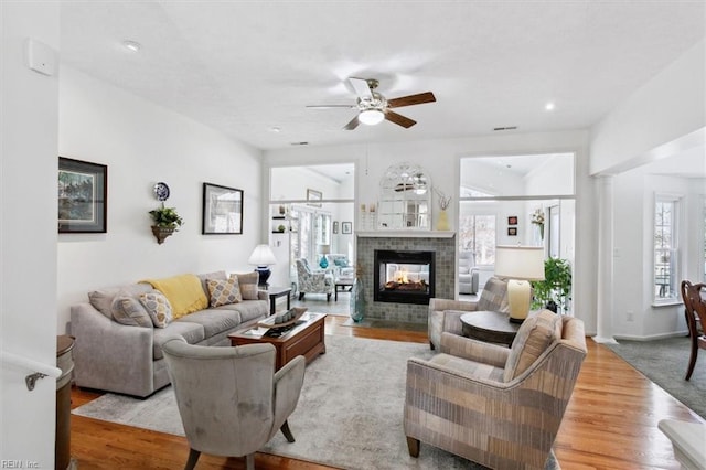 living room with baseboards, visible vents, a ceiling fan, wood finished floors, and a multi sided fireplace