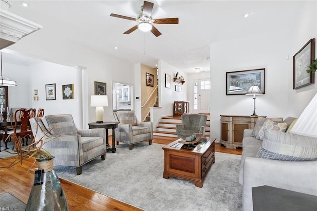 living area with stairway, ceiling fan, light wood-style flooring, and ornate columns