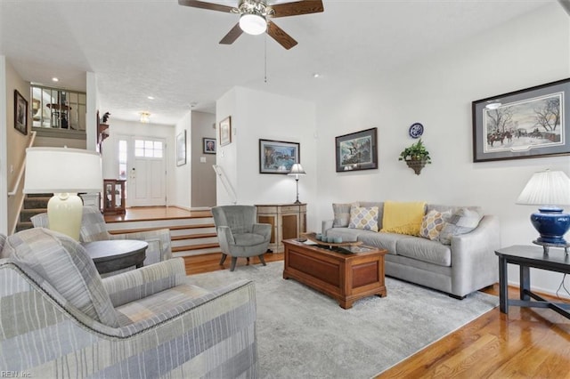 living area featuring baseboards, ceiling fan, light wood finished floors, and stairs