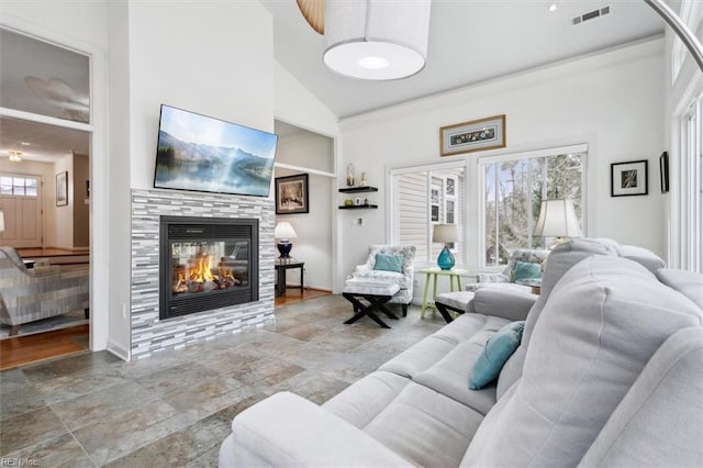 living area with high vaulted ceiling, a glass covered fireplace, visible vents, and baseboards