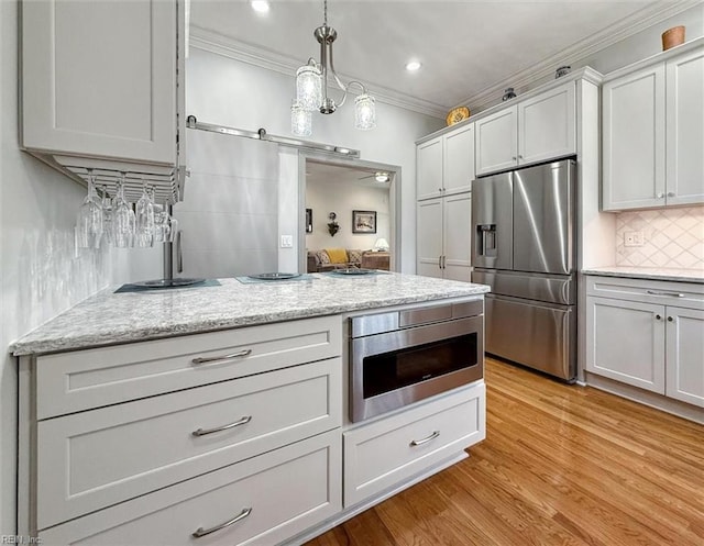 kitchen featuring a barn door, ornamental molding, appliances with stainless steel finishes, decorative backsplash, and light wood finished floors