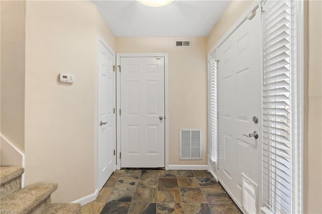 foyer with stone finish flooring, stairway, visible vents, and baseboards