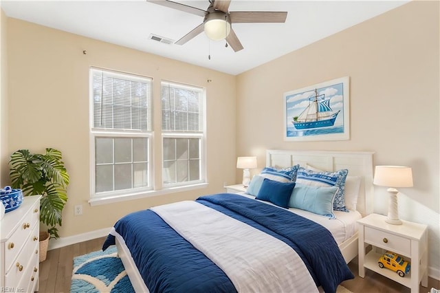 bedroom with ceiling fan, wood finished floors, visible vents, and baseboards