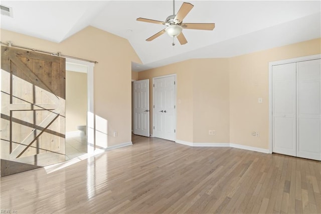 unfurnished bedroom with ceiling fan, a barn door, wood finished floors, baseboards, and vaulted ceiling