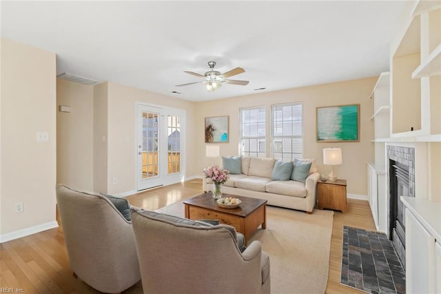 living area featuring visible vents, a ceiling fan, light wood-type flooring, baseboards, and a tile fireplace