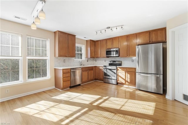 kitchen with light wood-style flooring, appliances with stainless steel finishes, light countertops, and backsplash