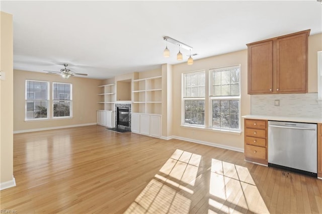 kitchen with tasteful backsplash, light countertops, stainless steel dishwasher, light wood-style floors, and a fireplace with flush hearth