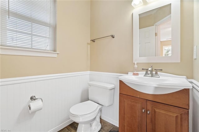 half bathroom with wainscoting, vanity, and toilet