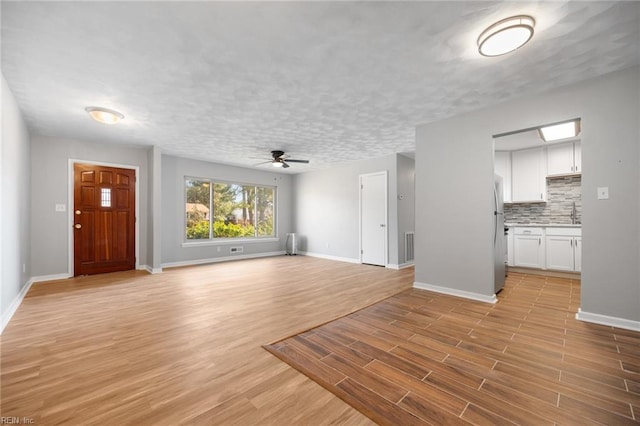 unfurnished living room with a textured ceiling, light wood finished floors, and baseboards