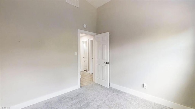 empty room featuring high vaulted ceiling, carpet, and baseboards