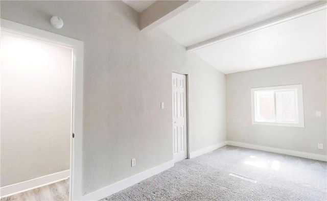 carpeted spare room featuring lofted ceiling with beams and baseboards